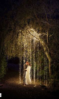 a bride and groom standing under a tree covered in lights