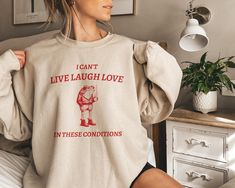 Hop into a world of humor and vintage vibes with our Funny Retro Frog Sweatshirt! Are you tired of the same old "live, laugh, love" mantra? Then this shirt is perfect for you! Crafted for those who appreciate a good chuck a dash of sarcasm, our 'I Can't Live Laugh Love In These Conditions' crewneck is sure to be a conversation starter. Made with high-quality materials, this pullover features a hipster frog, complete with a coffee mug, that embodies the soul of a true maverick. The design is prin Its Corn, Mountain Graphic Tee, Pogue Life, Comfy Crewneck, Lover Sweatshirt, Gifts For Farmers, Christian Sweatshirt, Cat Sweatshirt, Gildan Sweatshirts