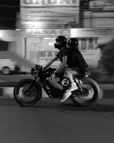 two people riding on the back of a motorcycle in front of a building at night