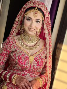 a woman in a red and gold bridal outfit with jewelry on her head, smiling at the camera