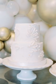 a white wedding cake sitting on top of a table next to gold and white balloons