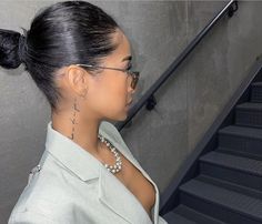 a woman with glasses and pearls on her neck standing in front of an escalator