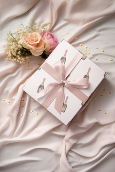 a gift box with a pink ribbon and flowers on a white bed sheet next to it