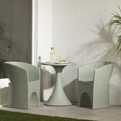 three chairs and a table in front of a white wall with grass on the ground