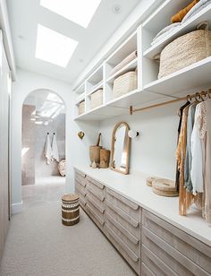 a walk in closet filled with lots of clothes and baskets on top of wooden shelves