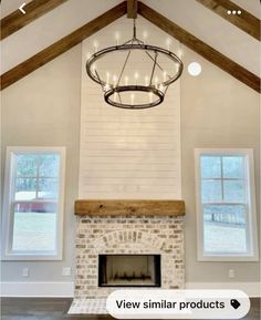 a chandelier hanging from the ceiling in a living room with two windows and a brick fireplace