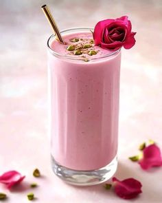 a pink smoothie in a glass with a rose on the top and petals around it