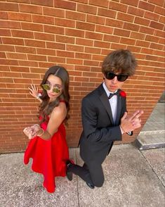 a boy and girl dressed up in formal wear standing next to each other on the sidewalk