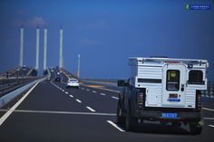 a white truck driving down a highway next to tall poles in the distance with traffic on both sides