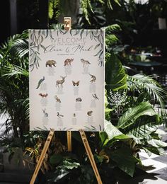 a welcome sign in front of some tropical plants and greenery on a wooden easel