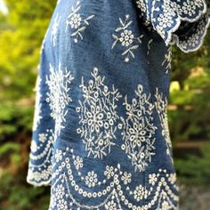 the back of a woman's blue top with white flowers on it, in front of trees