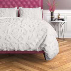 a white bed with pink headboard and pillows on top of wooden flooring in a bedroom