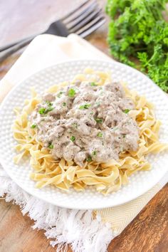 a white plate topped with pasta covered in meat sauce and garnished with parsley