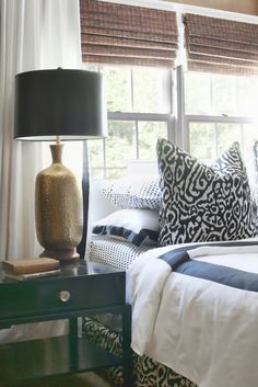 a bed sitting under a window next to a lamp on top of a wooden table