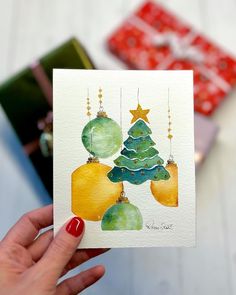 a hand holding up a christmas card with ornaments on it