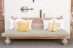 a wooden bench with pillows on it in front of a white door and brick wall