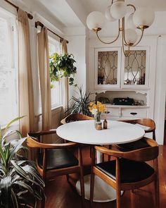 a dining room table and chairs with plants in vases on the top, next to two windows