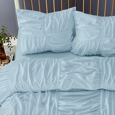 a bed with blue sheets and pillows on top of it in a room next to a potted plant