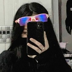 a woman with long black hair and sunglasses holding up her cell phone to take a selfie