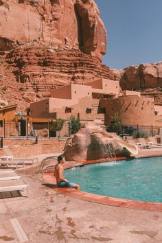 a man sitting on the edge of a swimming pool in front of a large rock formation