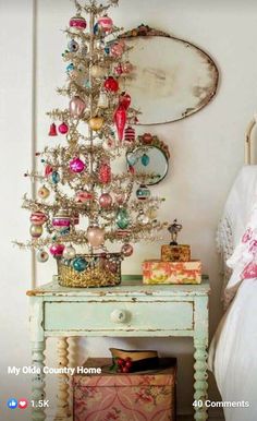 a small white christmas tree sitting on top of a wooden table next to a bed