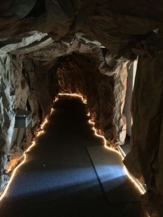 a long tunnel with lights on the sides and rocks all around it, leading to an entrance