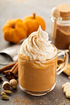 pumpkin spice latte with whipped cream in a glass mug and cinnamon sticks on the side