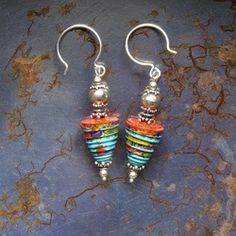 two pairs of colorful beads are hanging from silver earwires on a blue surface