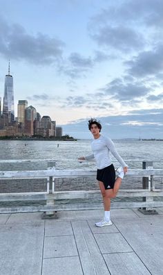 a woman standing on top of a wooden pier next to the ocean in front of a city skyline