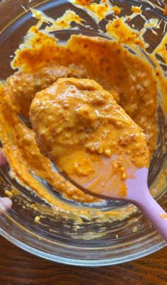 a spoon with some food in it on a glass bowl next to a wooden table