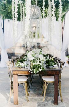 the table is set with white flowers and greenery hanging from it's ceiling