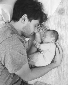 a man holding a baby in his arms while laying on top of a bed next to a pillow