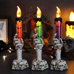 three lit candles in the shape of hands with skulls and bones on each candle holder