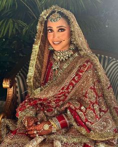 a woman in a red and gold bridal gown sitting on a couch with her hands clasped