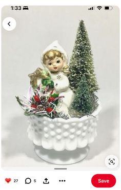 a small christmas tree in a white vase with a little angel on top and other decorations around the base