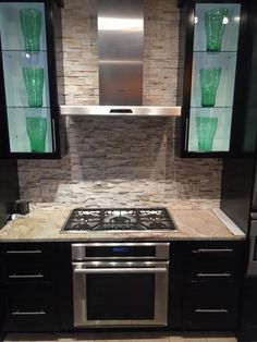 a stove top oven sitting inside of a kitchen next to cabinets and counter tops with green glass vases on it