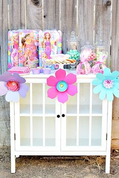 a white cabinet with paper flowers on top and candy in the back ground next to it