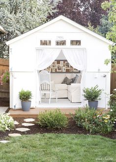 a small white shed with a couch in the corner and some plants on the side