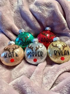 three christmas ornaments with names on them sitting next to a pink blanket and a white towel