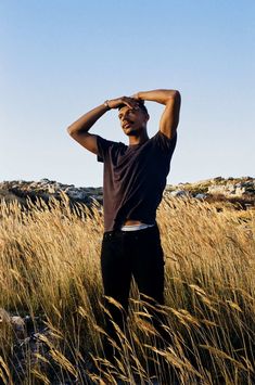 a man standing in tall grass with his hands on his head