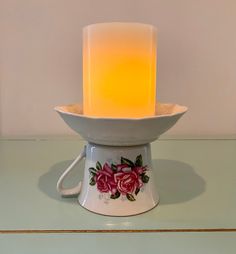 a lit candle sitting on top of a teacup with roses painted on it and the light is yellow