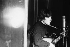 black and white photograph of a man playing guitar in front of a microphone on stage