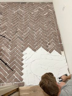 a man laying on the ground next to a wall with a brick pattern painted on it