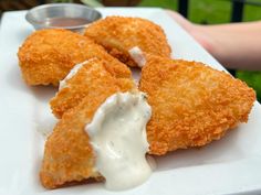 three fried chicken nuggets with ranch dip on a white plate in front of a person's hand