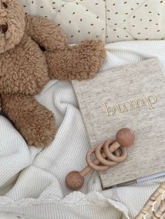 a brown teddy bear sitting on top of a bed next to a book and rattle