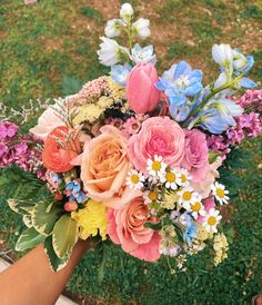 a bouquet of flowers is being held by someone's hand on the grass outside