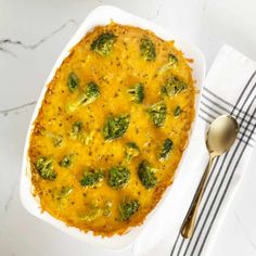 a casserole dish with broccoli and cheese in it next to a spoon