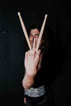 a man holding two wooden sticks in front of his face and making the v sign