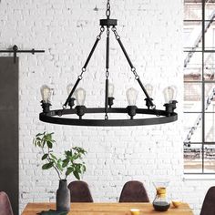 a dining room table and chairs in front of a white brick wall with an iron chandelier