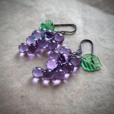 lilac grape earrings inspired by the fruit jewellery of the 1930's-1950's. lavender lilac grapes with emerald green leaves.  All parts are hand shaped  from molten glass and annealed in a digitally controlled kiln for extra durability. This colour shifts in different lighting.  a lavender-lilac in natural sunlight and pale blue in artificial light. They measure approx 1 7/8inch long, including the hooks, which are made of oxidised sterling silver.   *These earrings are made to order, so may diff Purple Glass Dangle Earrings, Nickel-free Purple Glass Jewelry, Fruit Jewellery, Glass Grapes, Grape Earrings, Fruit Jewelry, Artificial Light, Fruit Earrings, Earrings Inspiration